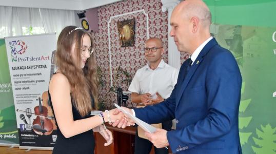 Absolwentka szkoły podstawowej odbiera nagrodę z rąk Burmistrza Arkadiusza Poprawy. W tle Dyrektor Szkoły Podstawowej w Pegowie Wojciech Wróbel.